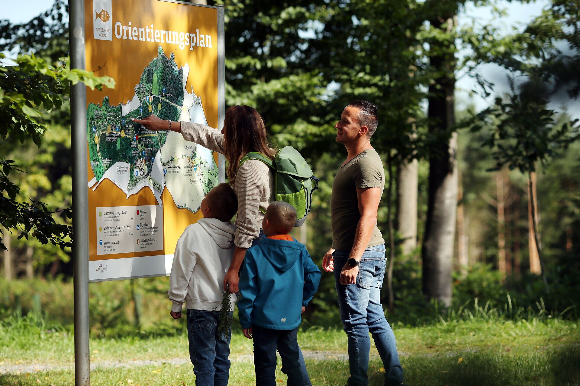 Eine Familie steht vor dem Orientierungsplan im Naturpark Geras, welcher auf einer großen Tafel abgebildet ist. 