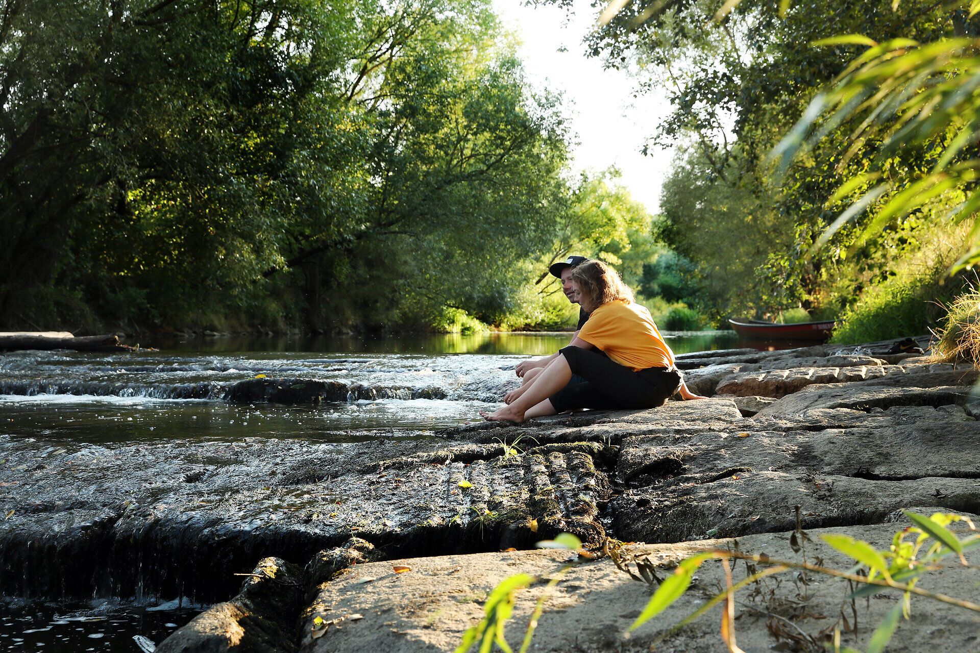 Ein Paar sitzt an der Thaya und hält die Füße ins Wasser. 