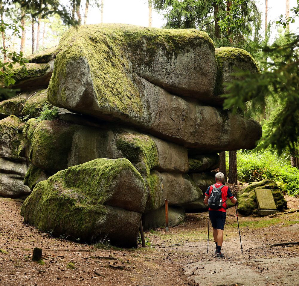 Ein Mann wandert neben einer großen Felsformation entlang eines Wanderweges. 