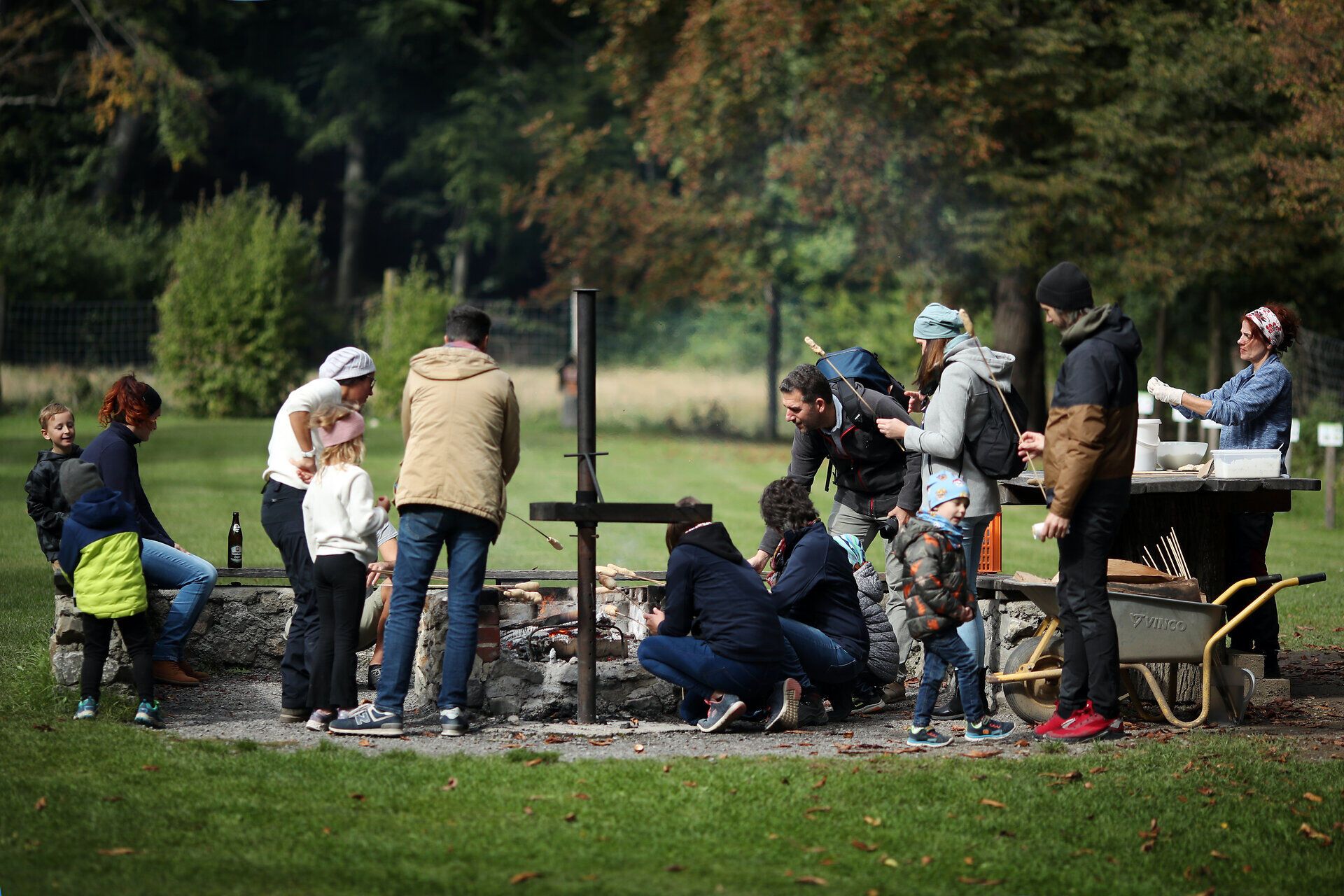 Eine große Gruppe an Leuten steht rund um den Grillplatz im Naturpark Sparbach. Einige davon grillen bereits Stockbrot. 