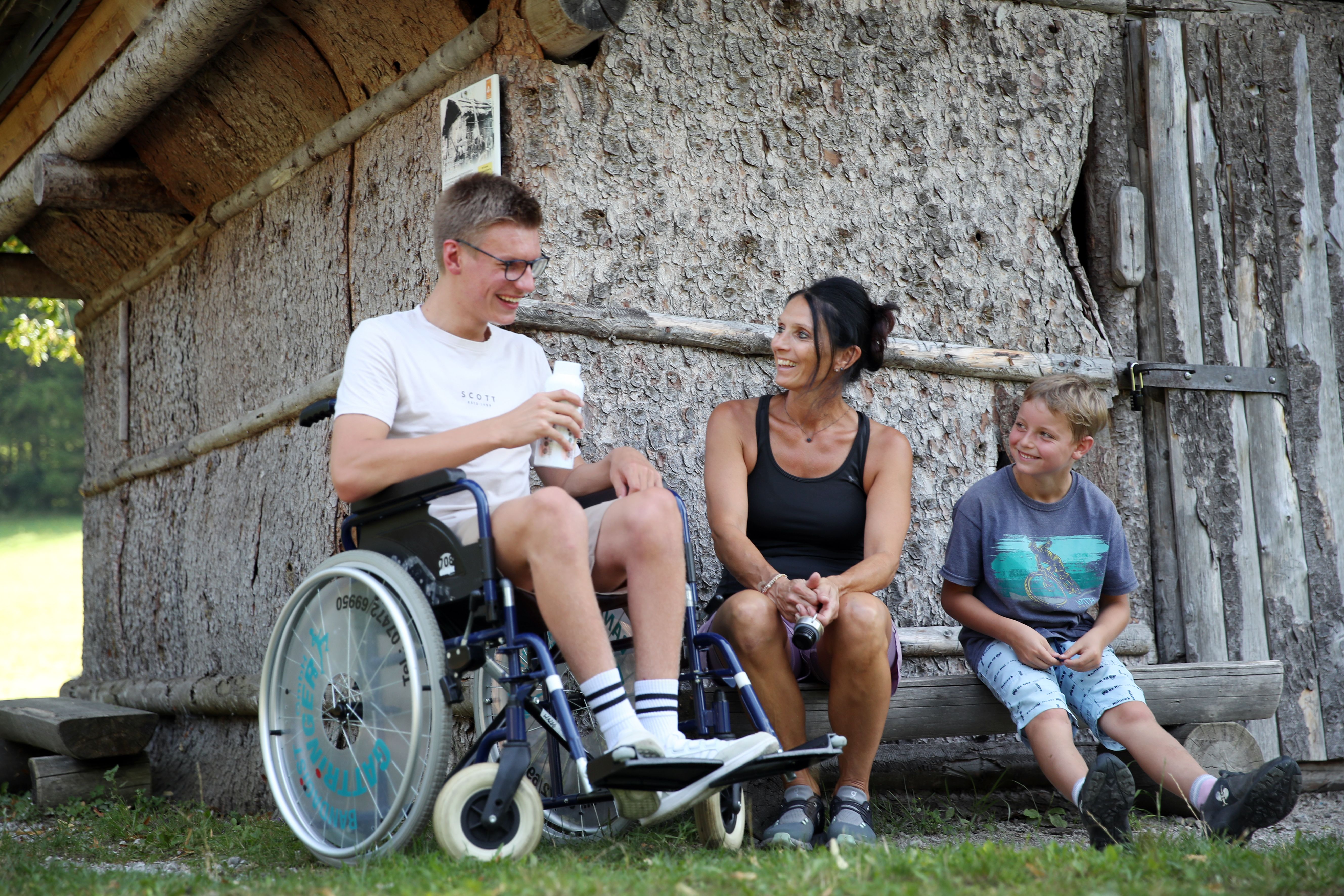 Junger Mann im Rollstuhl mit Freunden und Familie vor einer Hütte im Naturpark NÖ Eisenwurzen