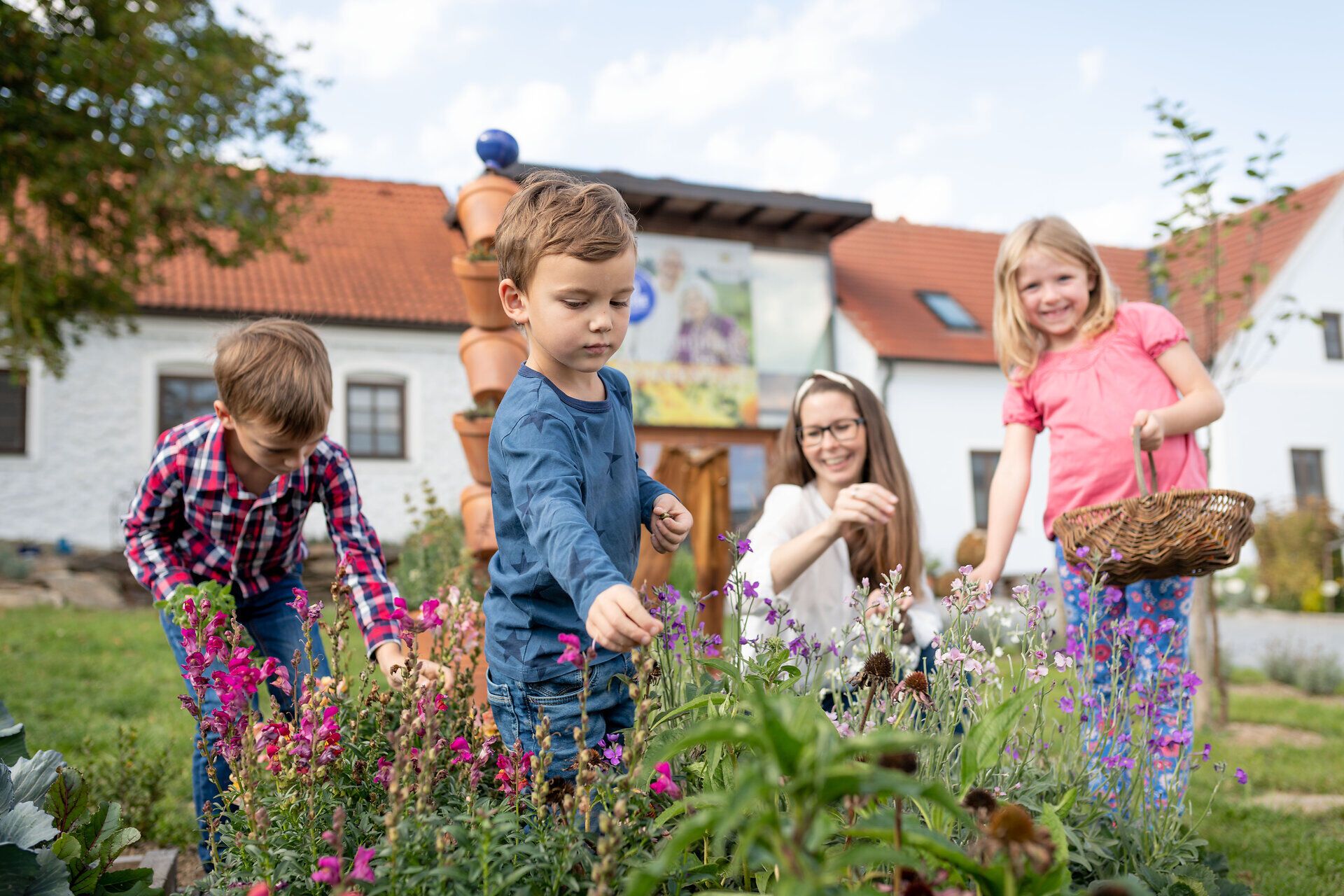 In einem bunten Kräutergarten sammeln fröhliche Kinder mit leuchtenden Augen die duftenden Blüten und Kräuter. Die warme Sonne strahlt auf die Familie, während sie gemeinsam die Natur entdecken und die Vielfalt der Pflanzen genießen. Ein harmonischer Moment, der die Freude am gemeinsamen Erleben in der Natur widerspiegelt.