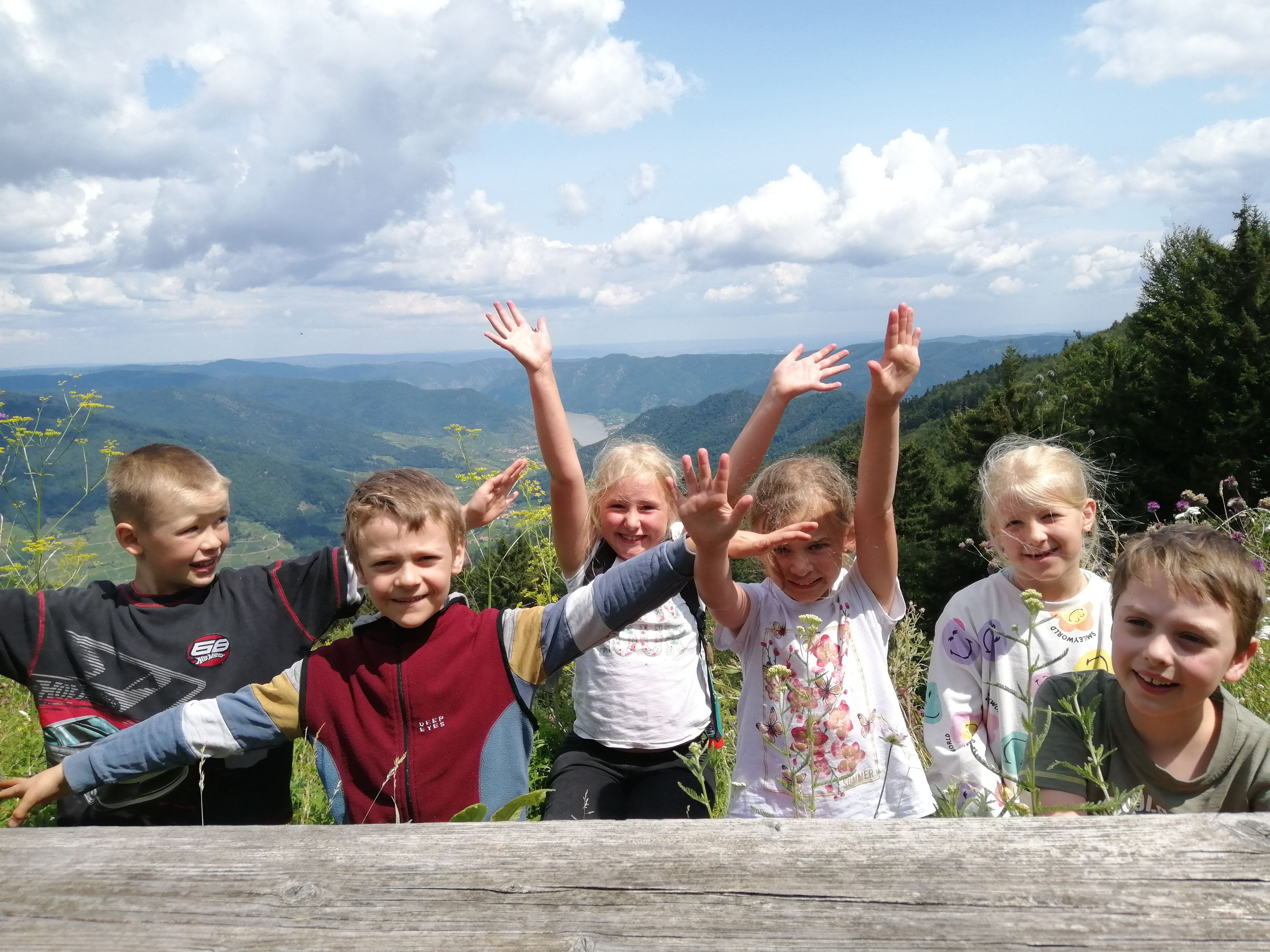 Mehrere Kinder winken glücklich in die Kamera, im Hintergrund sind die schönen Hügeln des Naturparks zu sehen.