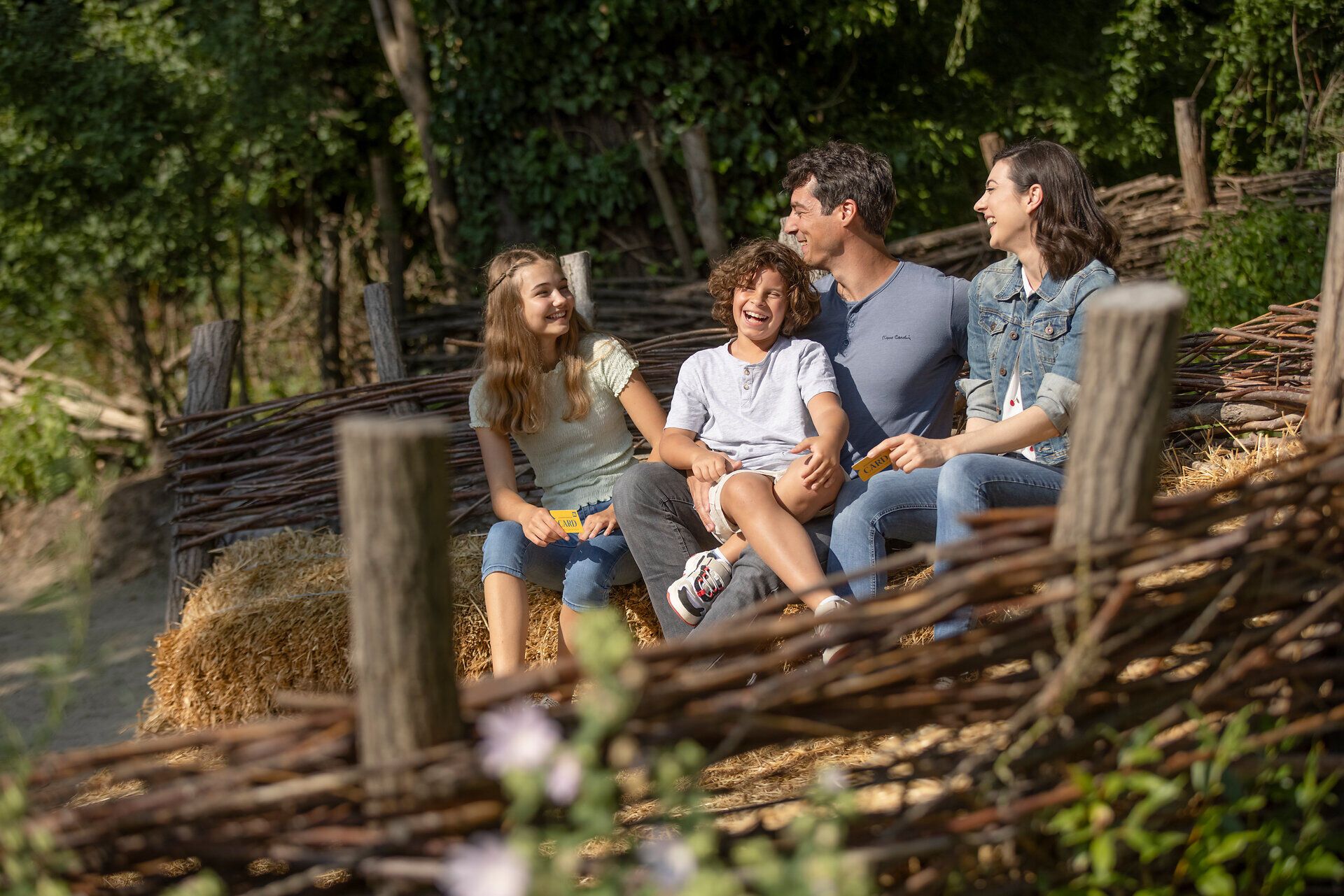Eine fröhliche Familie genießt die warmen Sonnenstrahlen und die entspannte Atmosphäre auf einem gemütlichen Platz im Freien. Umgeben von der Natur und dem rustikalen Charme von Strohballen und Holz, strahlt jeder ein Lächeln aus, während sie gemeinsam Zeit verbringen und die kleinen Freuden des Lebens feiern.